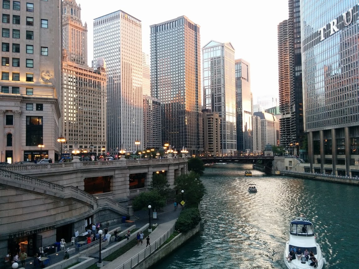 Boats sailing on a river between tall buildings in a cityscape at dusk.