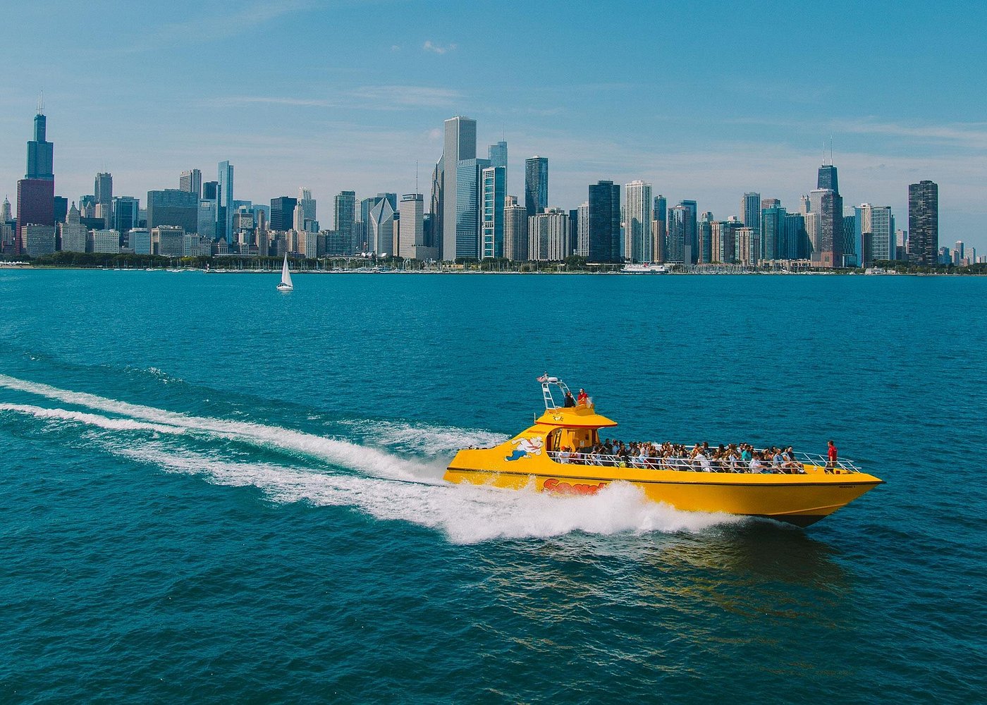 Yellow boat on blue water with city skyline in background under clear sky.