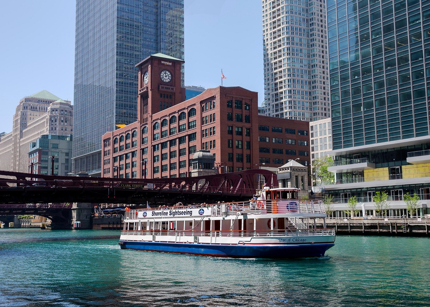Sightseeing boat on a river with city buildings and bridge in the background.