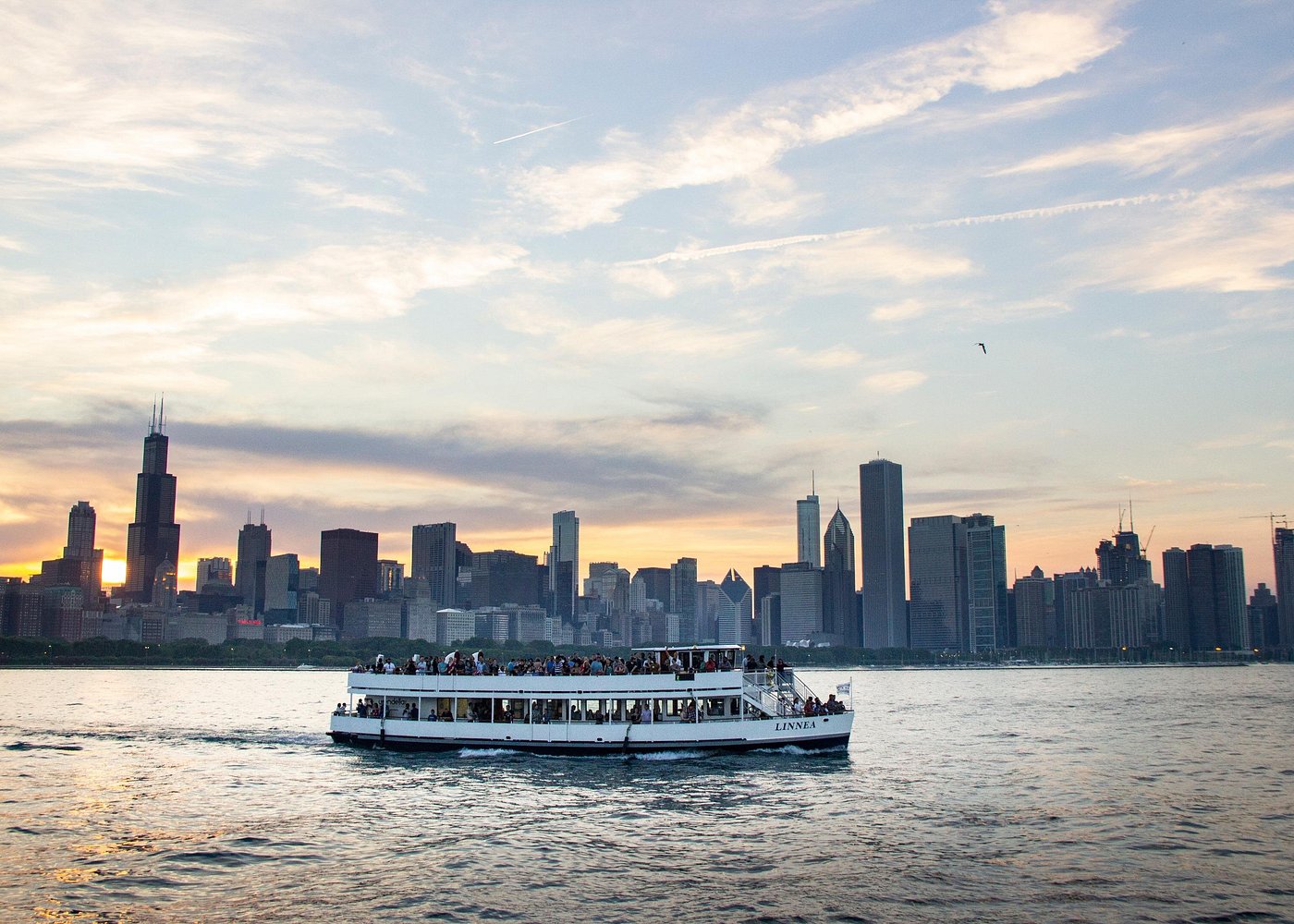 Boat on water with city skyline in background at sunset.